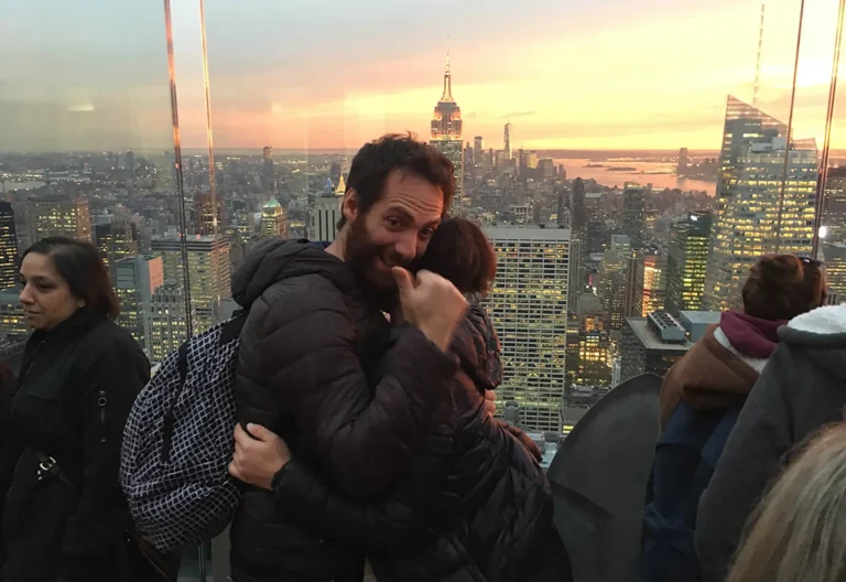 Uomo che sorride e abbraccia la partner dopo una proposta di matrimonio con lo skyline di New York sullo sfondo