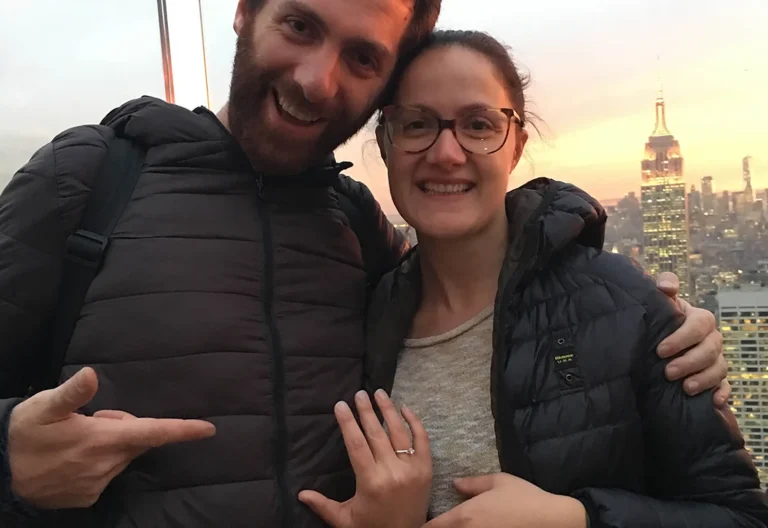 Coppia sorridente dopo la proposta di matrimonio con anello al dito e skyline di New York sullo sfondo