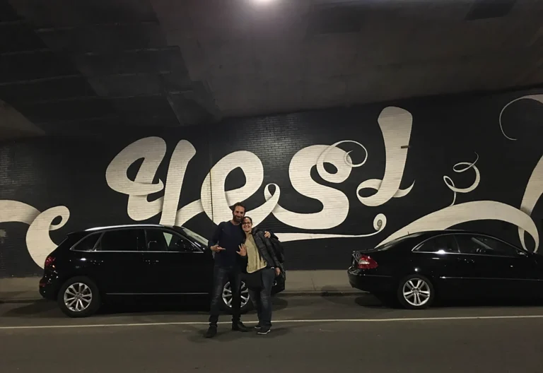 Coppia dopo la proposta di matrimonio davanti a un murale con la scritta Yes