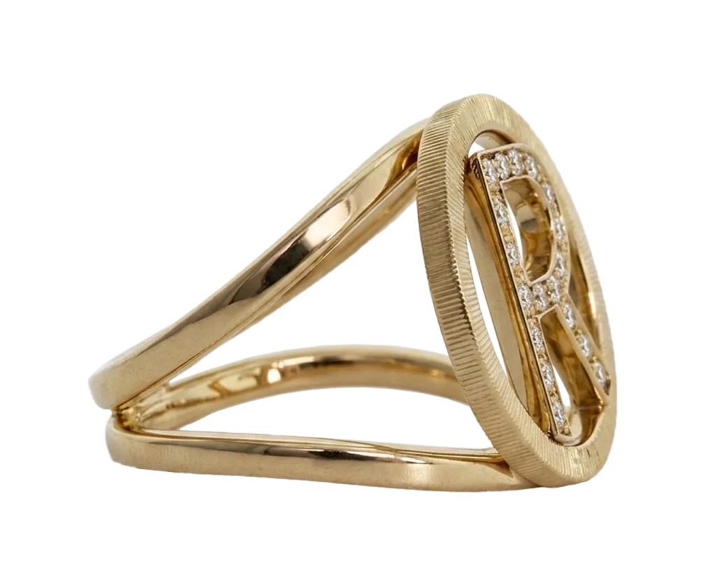 Front-facing photograph of the 18-carat yellow gold Initial ring. The view highlights the pave-set letter R, the open circular profile and the linear detailing of the outer edge.