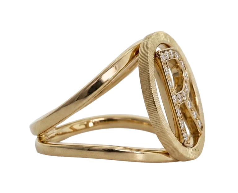 Front-facing photograph of the 18-carat yellow gold Initial ring. The view highlights the pave-set letter R, the open circular profile and the linear detailing of the outer edge.